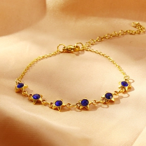 Détail du bracelet doré avec pierres bleues en forme d'étoile sur tissu en satin
