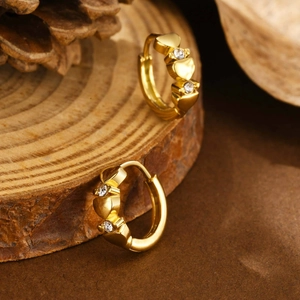 Close-up of golden heart-shaped hoop earrings with crystals on a wooden base