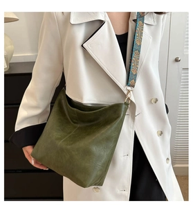 Detailed view of dark green soft leather tote with vintage patterned wide strap on a white coat