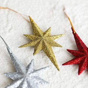 Set of glittery eight-pointed star Christmas ornaments in gold, silver, and red finishes