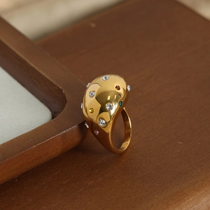 Golden geometric sphere ring with colorful gemstones on a warm wooden background
