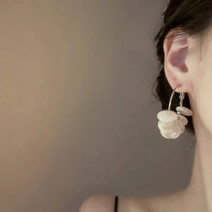 Close-up of a silver flower pearl hoop earring worn by a model in a black dress