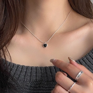 Close-up of a silver necklace featuring a black heart pendant on a female model