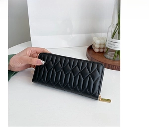 Close-up of black quilted long wallet with golden zipper on a wooden tray decor