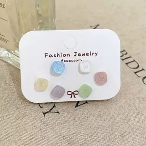 Close-up of six pairs of colorful square stud earrings on a fashion jewelry display card