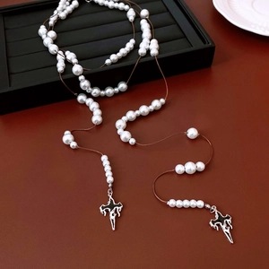 Detail of beaded glass cross necklace with long pearl chain and dark brown leather background