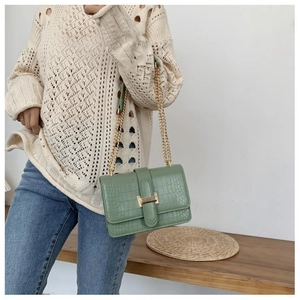 Close-up of a dark green crocodile pattern crossbody bag with a golden H-buckle