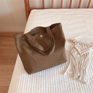 Close-up of brown canvas mini tote bag with metal snap button on white quilted bed