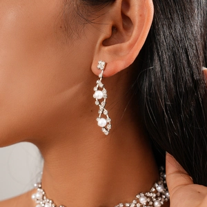 Detailaufnahme eleganter silberfarbener Blumenohrringe und Perlenkette mit Strasssteinen