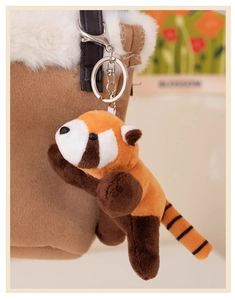 Close-up of a cute plush red panda keychain hanging on a brown bag strap with metal ring