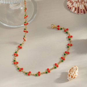 Detail of a golden cherry charm bracelet with red fruit and green leaves on a beige surface