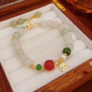 Close-up of beaded bracelet with green jade, red bead and gold lucky charm on wood box
