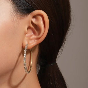 Detail of gold large hoop earrings with baguette-cut zircons worn by a female model