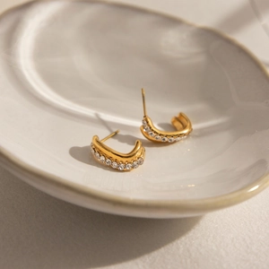 Close-up of gold-plated double twisted C-hoop earrings with sparkling rhinestones