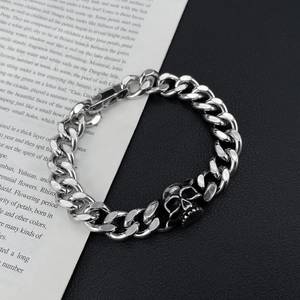 Close-up of silver Cuban link bracelet with skull charm over an open book and black surface