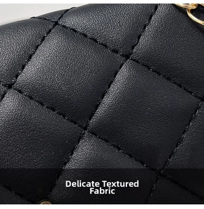 Close-up of black quilted leather texture and golden metal chain detail on the square bag