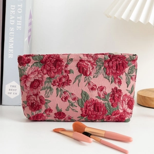 Close-up of vintage floral cosmetic bag with red roses and makeup brushes on a desk