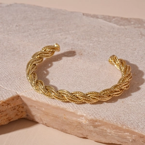 Detailed close-up of a gold twisted cuff bracelet on a natural stone textured background