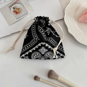 Close-up of black paisley drawstring pouch with cosmetics on a minimalist desktop