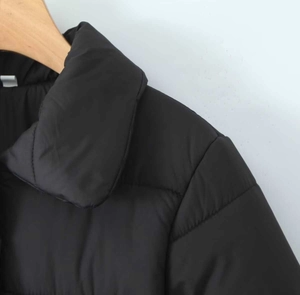 Dettaglio del piumino nero con cappuccio che mostra il tessuto opaco e le cuciture su gruccia