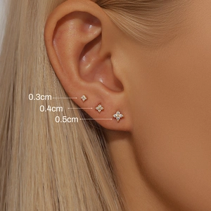 Three sizes of gold flower stud earrings with white rhinestones shown on ear