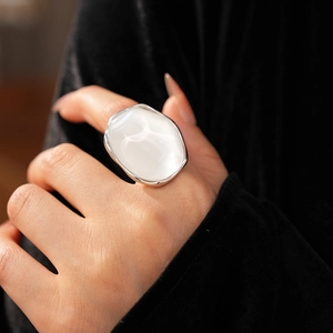 Close-up of a silver oval resin ring with a white cat's eye stone on a black background