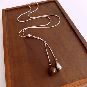 Détail de pendentifs gouttes argentés sur un collier chaîne serpent et plateau bois