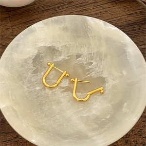 Macro shot of minimalist gold U-shaped horseshoe stud earrings on white stone display