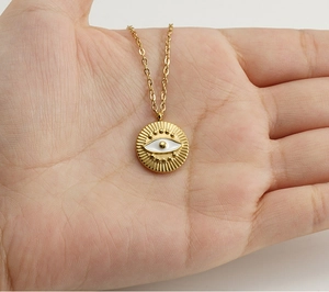 Close-up of golden stainless steel necklace with evil eye pendant held in palm