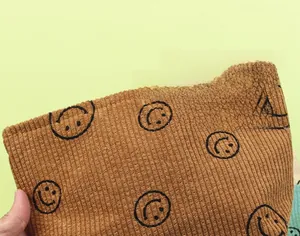 Detail of brown corduroy makeup bag with black smiley patterns and ribbed texture