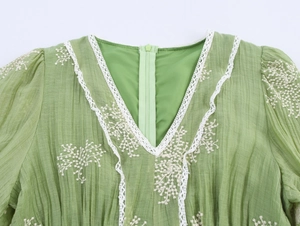 Close-up of green V-neck dress with white floral embroidery and delicate lace trim