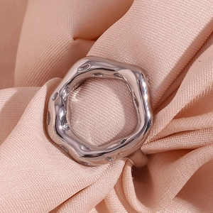 Close-up of irregular silver wavy metal ring displayed on smooth satin fabric