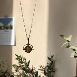 Detailed view of a vintage gold coin pendant necklace hanging against a soft warm background