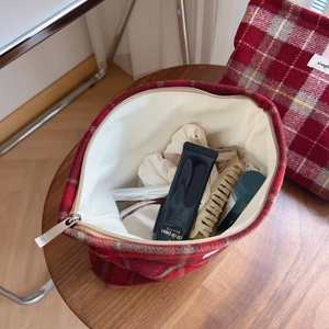 Trousse à maquillage en laine à carreaux écossais rouges posée sur une table en bois