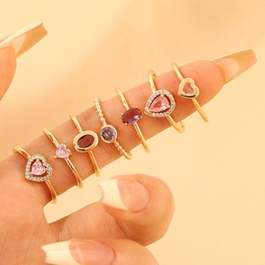 Close-up of set of 7 gold rings with pink and purple zircon stones on fingers