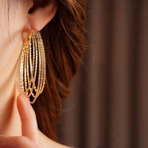 Close-up of layered golden hoop earrings with textured finish on model showing high shine