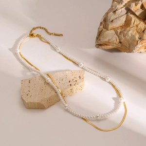 Double-layer gold snake chain and pearl necklace displayed on decorative natural stones