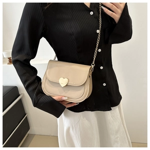 Model wearing a beige patent leather saddle bag with gold heart lock and chain strap