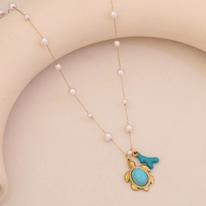 Elegant gold pearl necklace with turtle and blue coral pendants on a neutral stone base