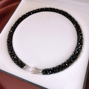 Macro shot of faceted black glass beads and a silver pavé-set spherical clasp in a jewelry box