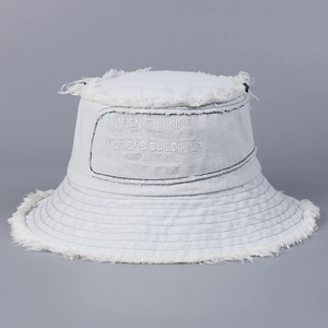 Dettaglio dei bordi sfrangiati e dei ricami bianchi sul cappello a secchiello in denim
