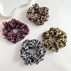 Set of four leopard print satin scrunchies in purple, white, and khaki on a minimalist tray