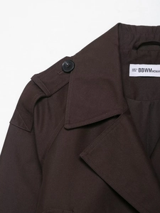 Detail eines dunkelbraunen Trenchcoats mit Schulterklappen und Twill-Gewebe