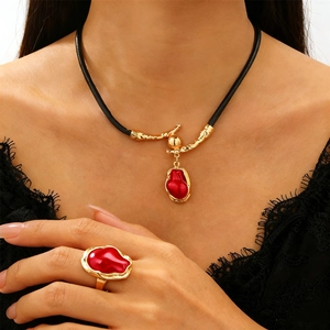 Dettaglio di set collana e anello barocco dorato con gemme rosse e cordino in pelle