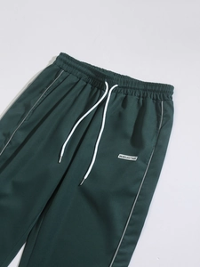 Detail of deep green woven joggers featuring elastic waist with white contrast drawstrings
