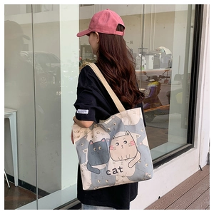 Outdoor street style view of a canvas tote bag with cartoon cat patterns on a model