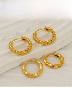 Close-up of gold-plated stainless steel twisted and wavy hoop earrings on a white stand