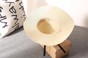 Detail of a beige woven wide brim straw hat with elegant black ribbon decoration