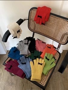 Knitted winter gloves with bow accents in multiple colors on a stylish rattan chair