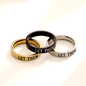 Close-up of titanium steel rings in gold, black, and silver with 'LET THEM' engraving